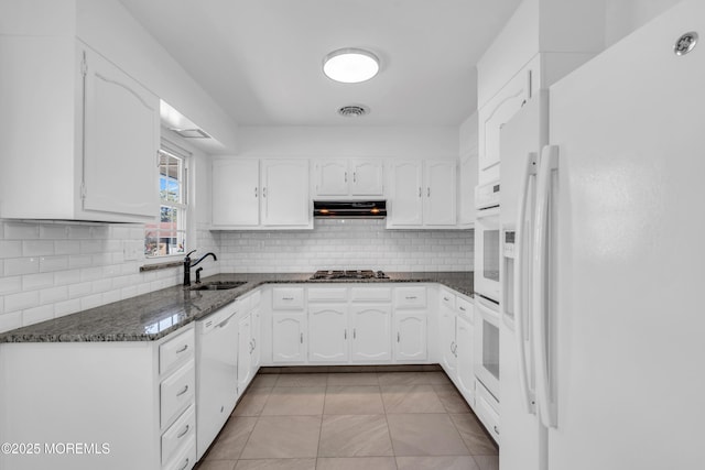 kitchen with under cabinet range hood, dark stone countertops, white cabinets, white appliances, and a sink