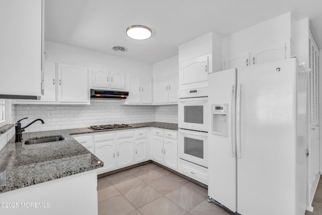 kitchen featuring white appliances, dark stone counters, a sink, under cabinet range hood, and white cabinetry