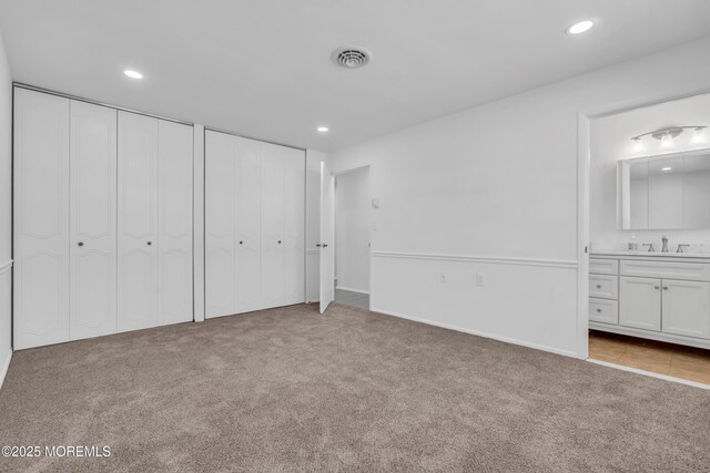 unfurnished bedroom featuring a sink, visible vents, carpet floors, and two closets