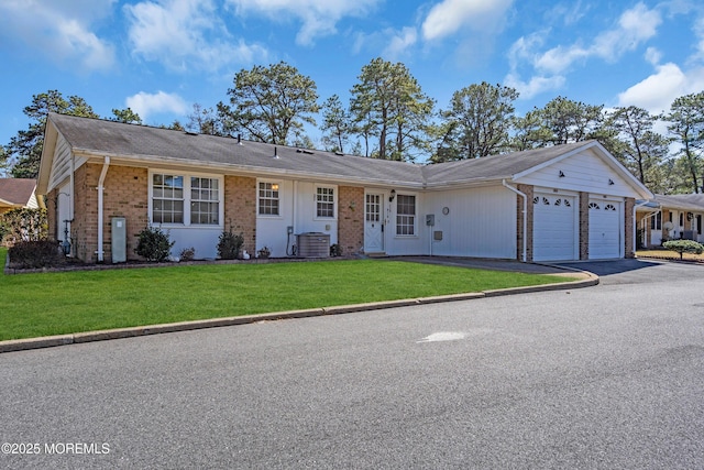 single story home featuring brick siding, a front lawn, central air condition unit, driveway, and an attached garage