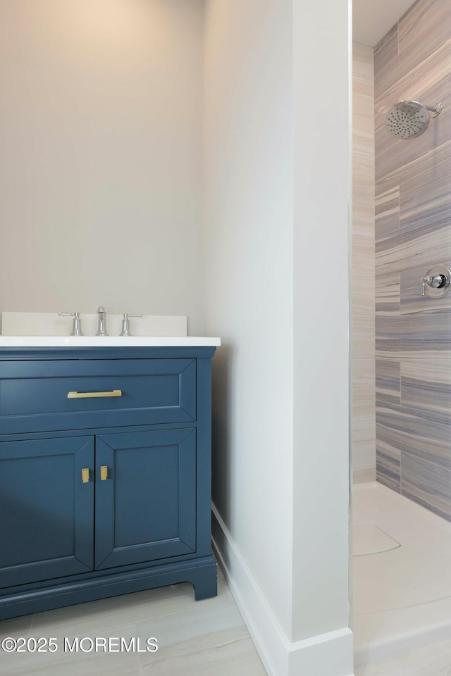 full bath with tiled shower, vanity, and baseboards