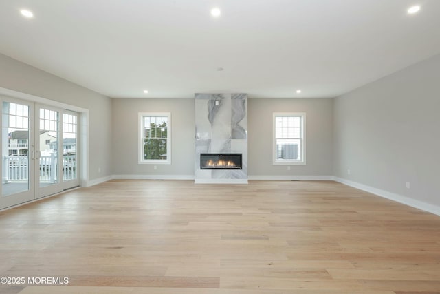 unfurnished living room featuring light wood finished floors, a premium fireplace, plenty of natural light, and baseboards