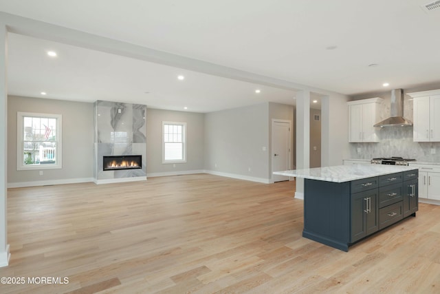 kitchen with light wood-style flooring, decorative backsplash, a premium fireplace, a kitchen island, and wall chimney exhaust hood