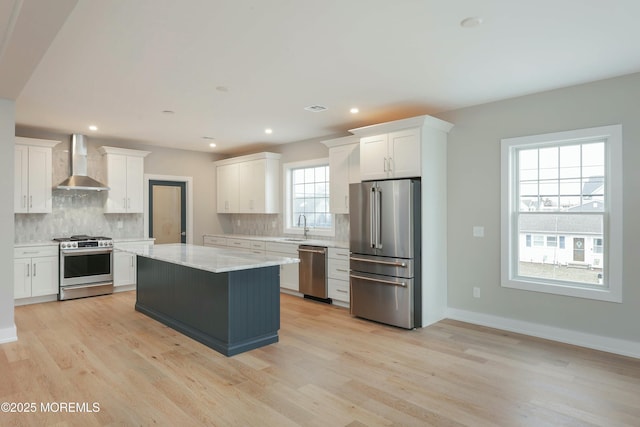 kitchen featuring white cabinets, wall chimney exhaust hood, appliances with stainless steel finishes, light wood-type flooring, and a sink