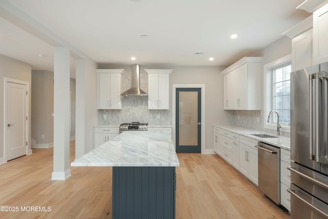 kitchen with a kitchen island, stainless steel appliances, light wood-type flooring, wall chimney range hood, and a sink