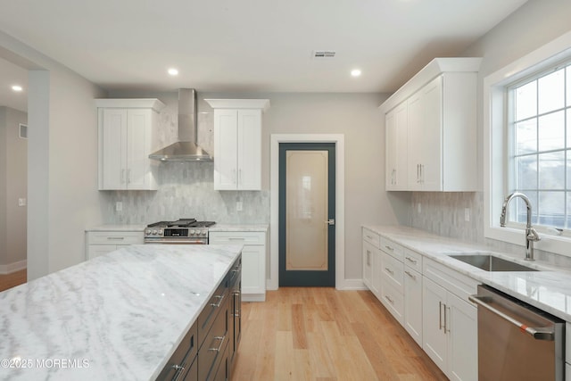 kitchen featuring visible vents, appliances with stainless steel finishes, white cabinetry, a sink, and wall chimney range hood