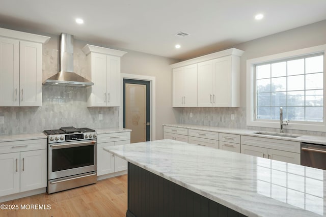 kitchen with light wood-style flooring, a sink, white cabinetry, appliances with stainless steel finishes, and wall chimney exhaust hood