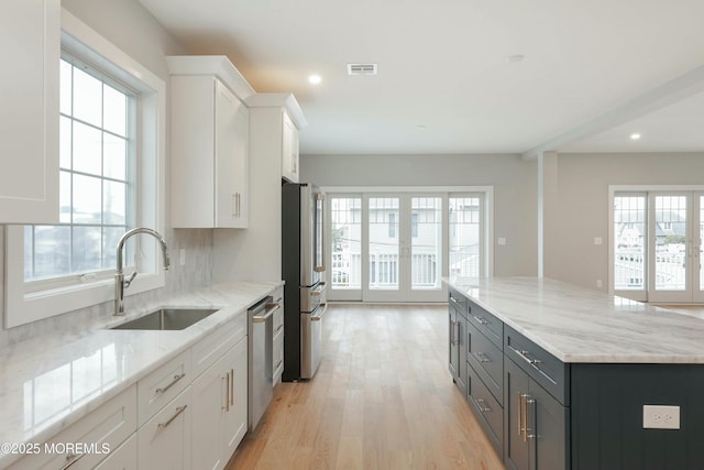 kitchen with light wood-style flooring, stainless steel appliances, a sink, visible vents, and white cabinets