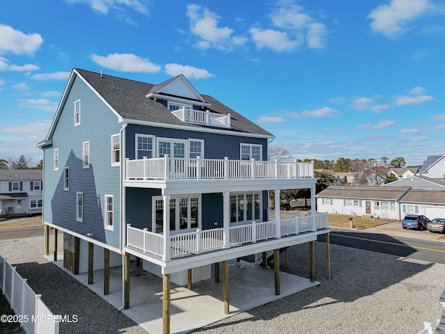 rear view of house featuring a residential view, a patio area, roof with shingles, and a balcony