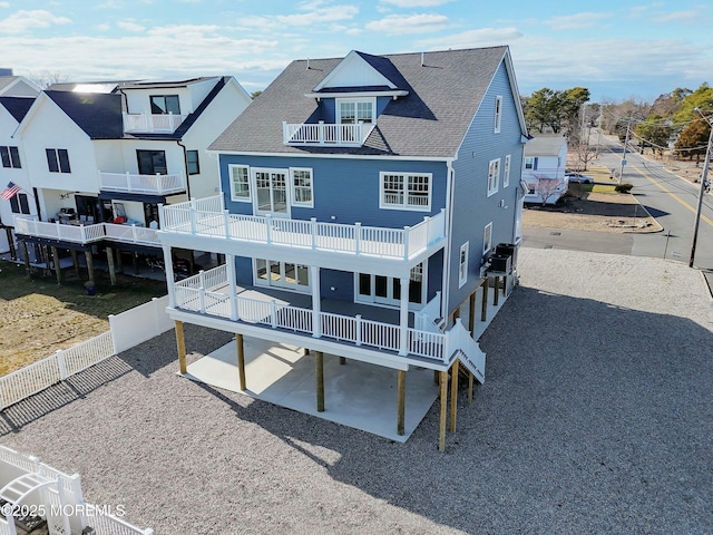 back of property with a shingled roof, a patio, a balcony, a fenced backyard, and gravel driveway