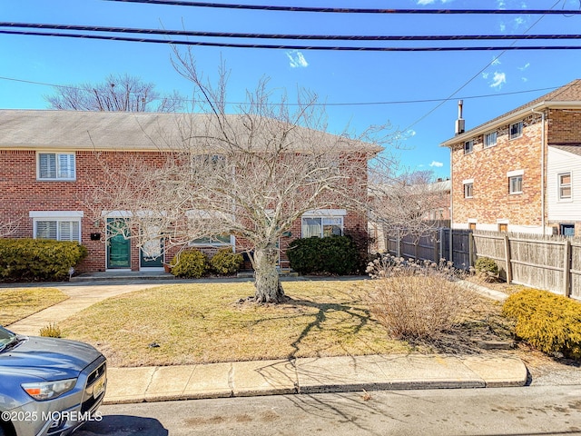 view of front of house with brick siding, a front yard, and fence