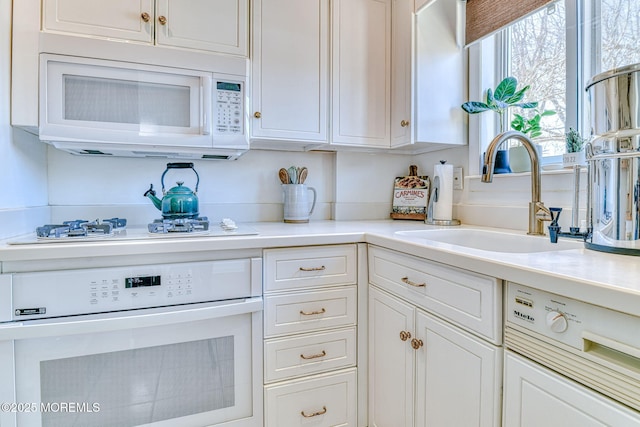 kitchen featuring a sink, white appliances, white cabinets, and light countertops