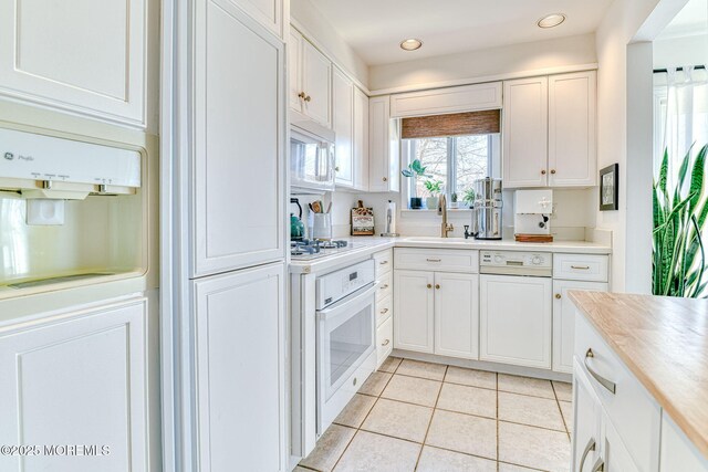 kitchen featuring white appliances, light tile patterned floors, a sink, light countertops, and white cabinetry