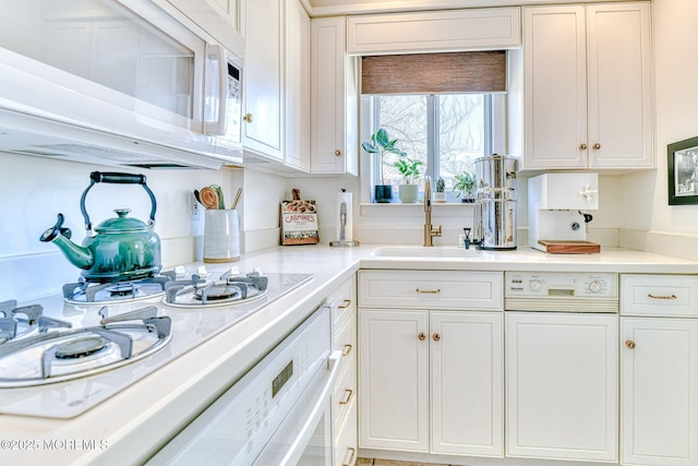 kitchen featuring white microwave, white cabinets, light countertops, and a sink