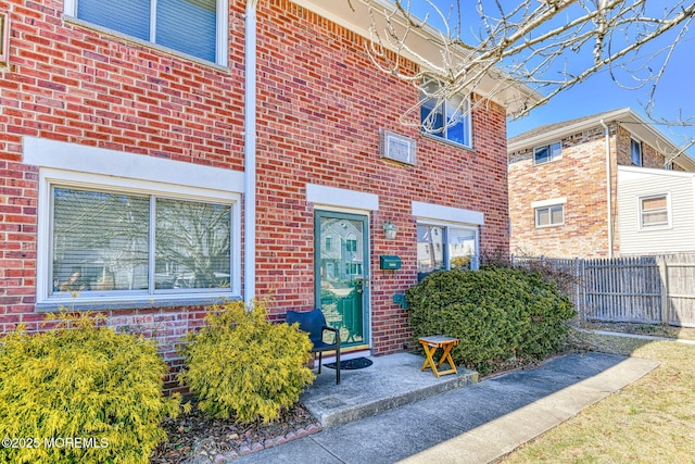 view of exterior entry featuring brick siding and fence