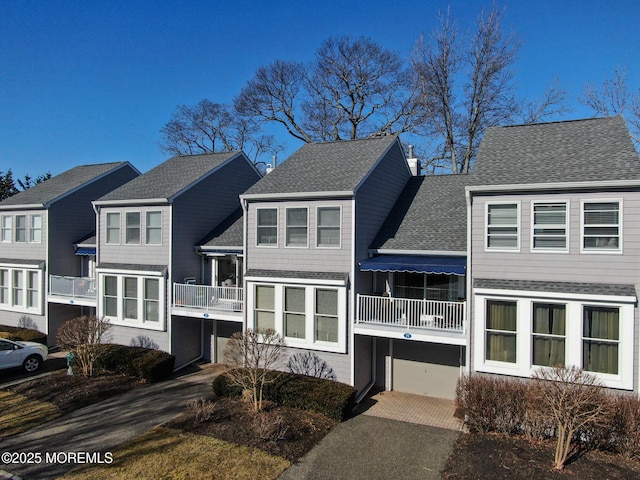 view of front of property with a garage, driveway, a shingled roof, and a balcony