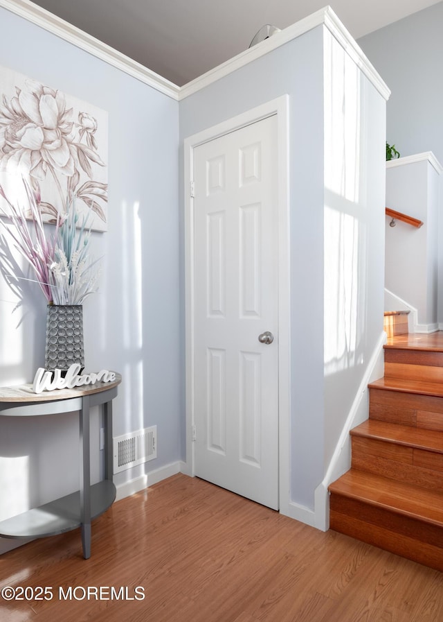 interior space with visible vents, ornamental molding, wood finished floors, baseboards, and stairs