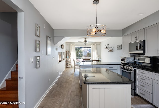 kitchen with a peninsula, wood finished floors, baseboards, appliances with stainless steel finishes, and dark stone counters