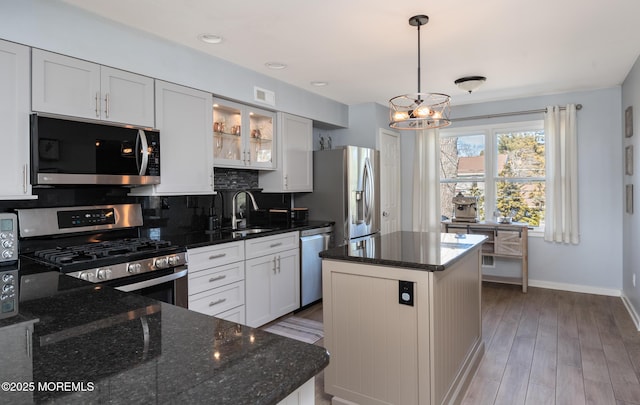 kitchen featuring tasteful backsplash, appliances with stainless steel finishes, wood finished floors, a center island, and a sink