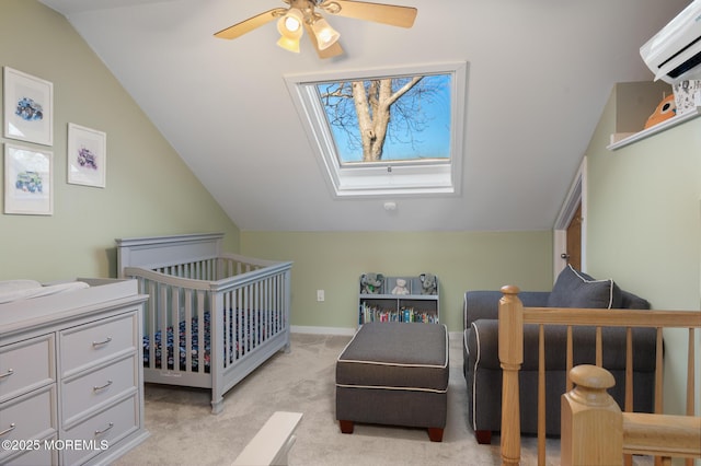 bedroom featuring light carpet, vaulted ceiling with skylight, a ceiling fan, a wall mounted air conditioner, and a nursery area