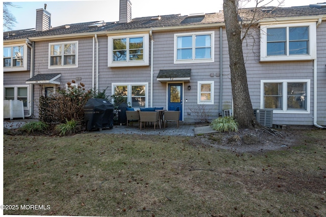 rear view of property featuring a chimney, a patio, central AC unit, and a lawn