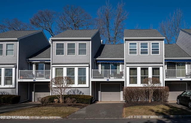 multi unit property featuring a garage, aphalt driveway, roof with shingles, and a balcony