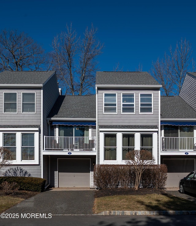 view of front facade featuring a garage, aphalt driveway, roof with shingles, and a balcony