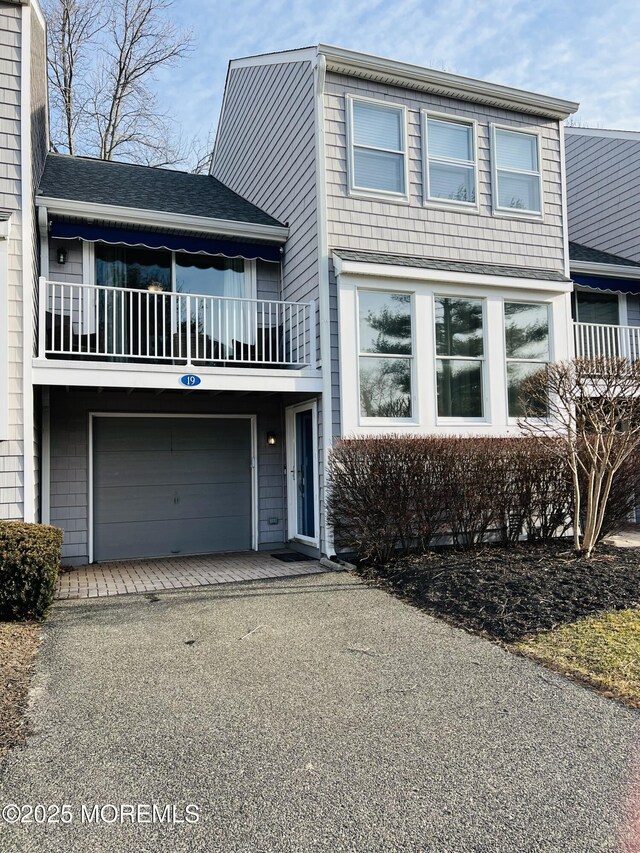 view of front of house with a balcony, driveway, a garage, and roof with shingles