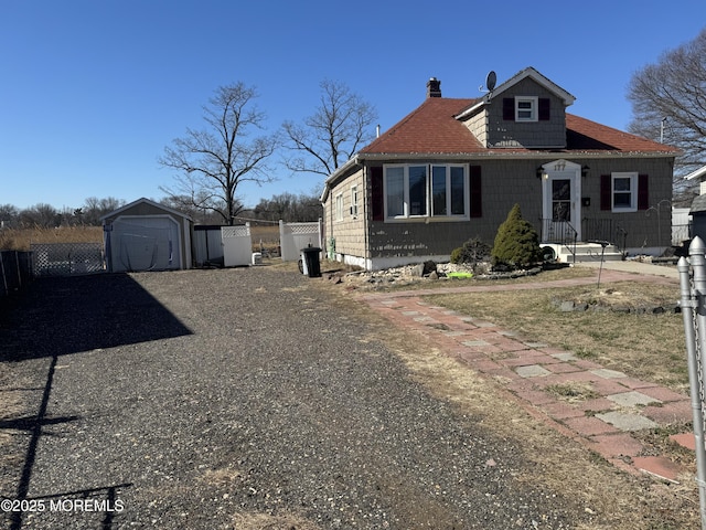 view of front of home featuring an outbuilding, fence, driveway, and a chimney