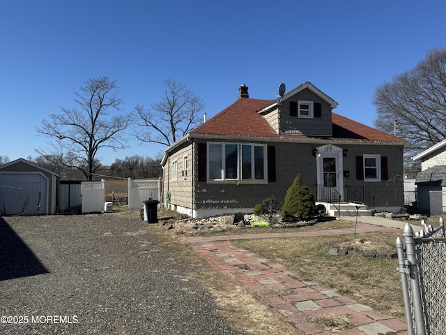 bungalow-style home featuring fence, driveway, a shed, a chimney, and an outdoor structure