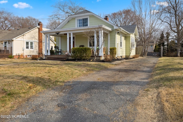 bungalow-style home featuring a chimney, roof with shingles, a porch, and a front yard