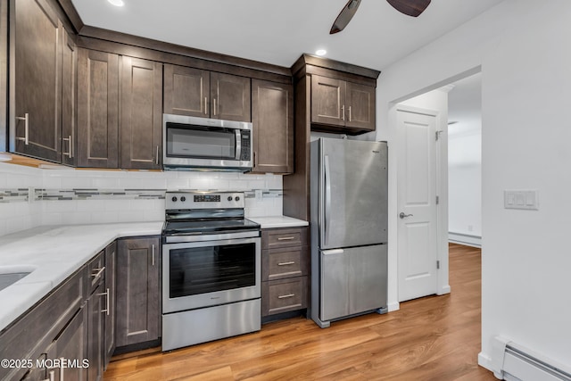 kitchen featuring light wood-type flooring, a baseboard radiator, dark brown cabinets, appliances with stainless steel finishes, and tasteful backsplash