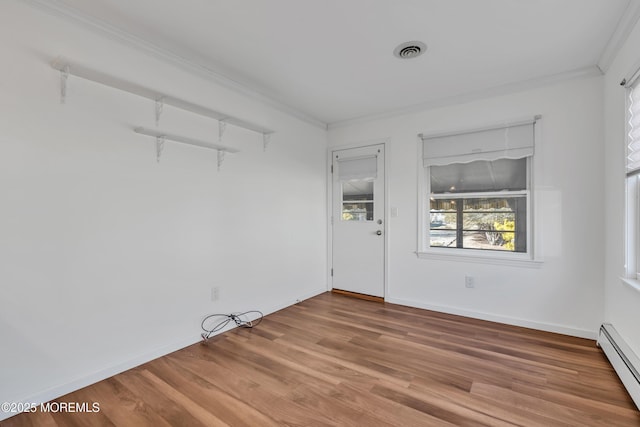 empty room featuring visible vents, a baseboard heating unit, wood finished floors, crown molding, and baseboards