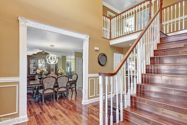 stairway with crown molding, a decorative wall, a high ceiling, wainscoting, and wood finished floors