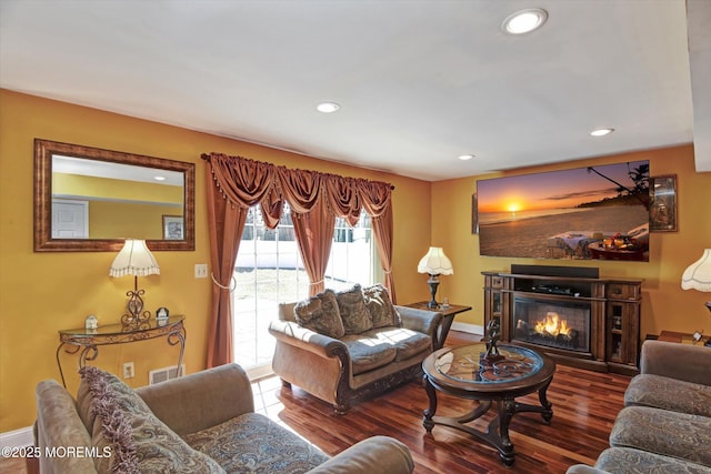 living room featuring baseboards, a glass covered fireplace, wood finished floors, and recessed lighting