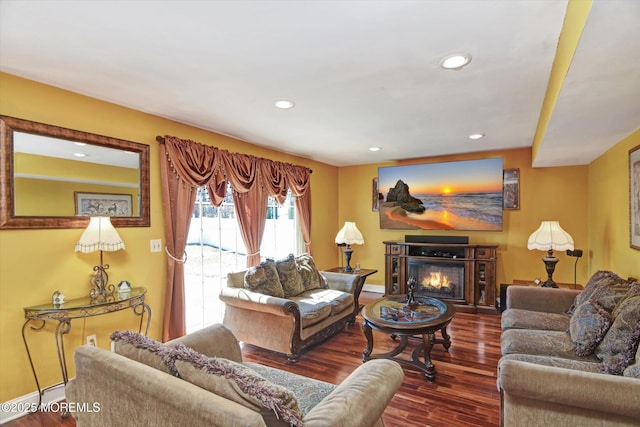 living area featuring recessed lighting, baseboard heating, a glass covered fireplace, wood finished floors, and baseboards