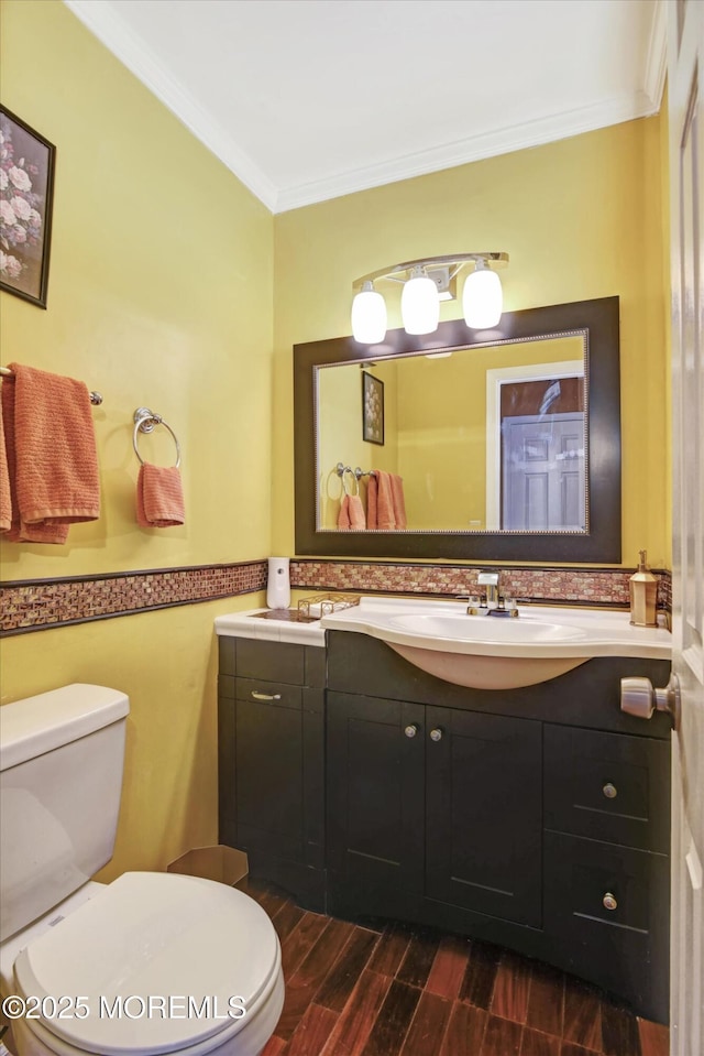 half bathroom with vanity, wood finished floors, toilet, and crown molding