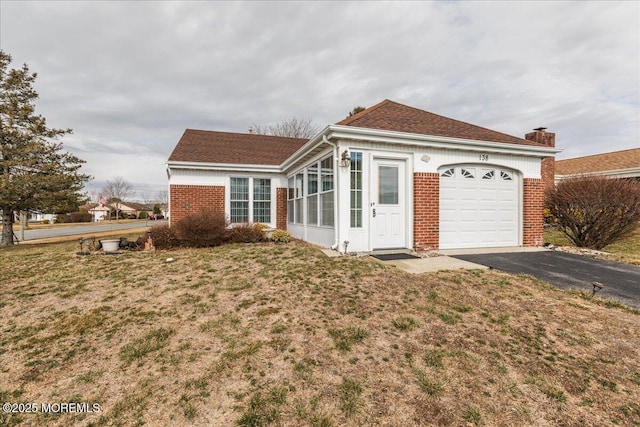 view of front of property featuring a garage, brick siding, a front lawn, and aphalt driveway