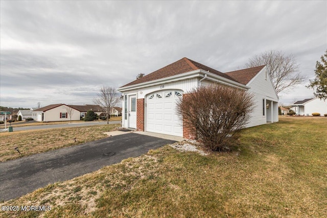 view of side of home with a garage, aphalt driveway, a lawn, and brick siding