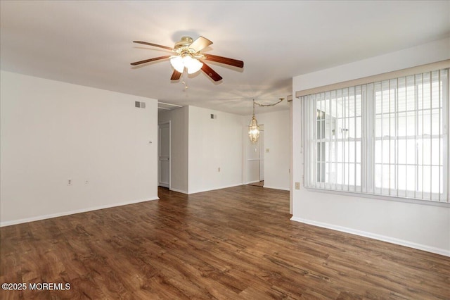 empty room featuring baseboards, visible vents, dark wood finished floors, and ceiling fan with notable chandelier