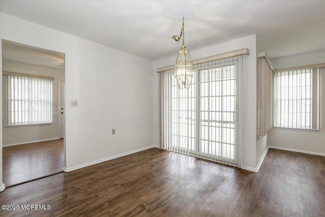 unfurnished dining area with a healthy amount of sunlight, an inviting chandelier, baseboards, and wood finished floors