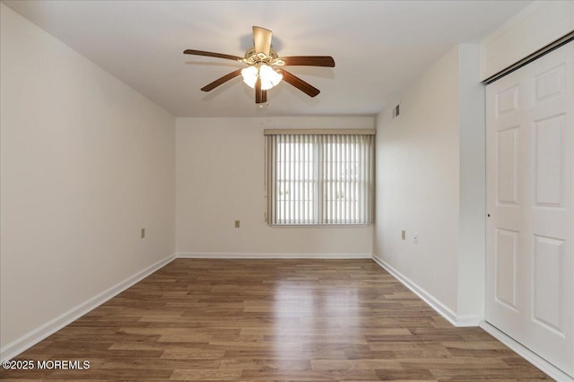 empty room with a ceiling fan, visible vents, baseboards, and wood finished floors