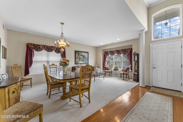 dining space with baseboards, light wood finished floors, ornate columns, and an inviting chandelier