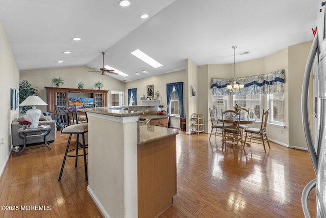 kitchen featuring vaulted ceiling with skylight, visible vents, open floor plan, light wood-type flooring, and stainless steel refrigerator