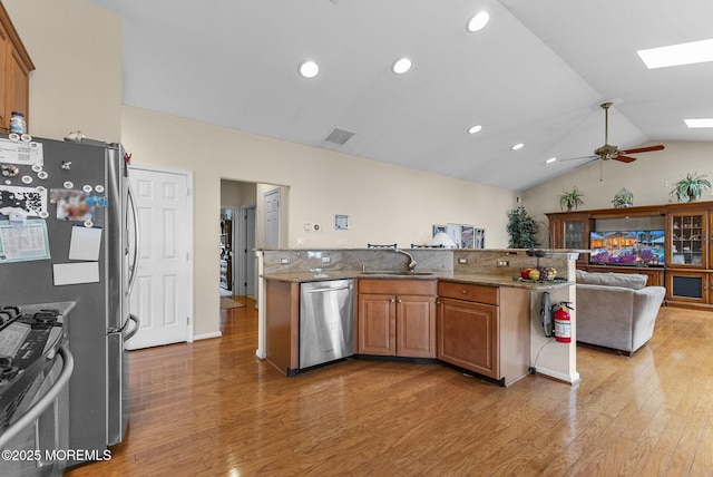 kitchen with light wood-style floors, vaulted ceiling with skylight, appliances with stainless steel finishes, and a sink