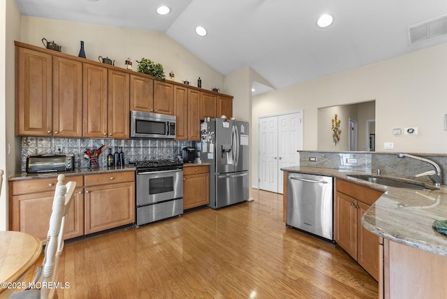 kitchen with stainless steel appliances, lofted ceiling, visible vents, a sink, and light stone countertops