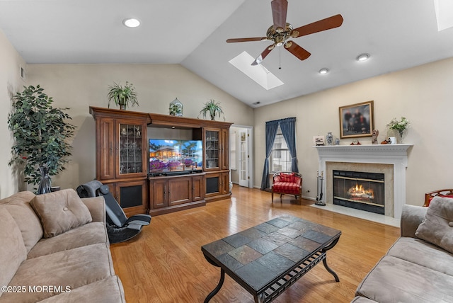 living room with vaulted ceiling with skylight, light wood-style flooring, recessed lighting, a premium fireplace, and a ceiling fan