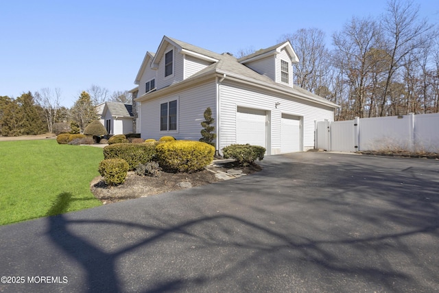 view of side of property featuring a garage, aphalt driveway, a gate, fence, and a yard