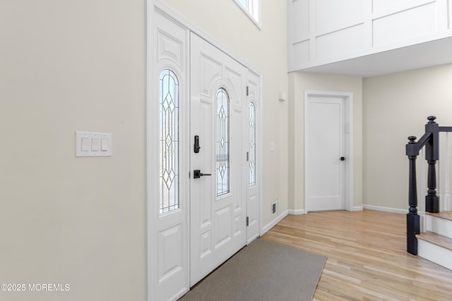 foyer with baseboards, a towering ceiling, and light wood-style floors