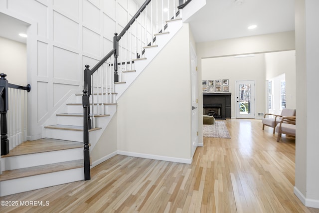 stairway featuring baseboards, a towering ceiling, wood finished floors, a fireplace, and recessed lighting